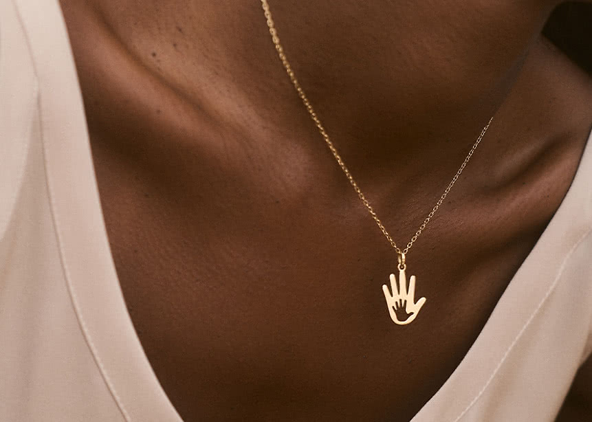 A woman wearing a necklace shaped like a hand in 18K Yellow Gold from the VANBRUUN x CHILDHOOD collection.